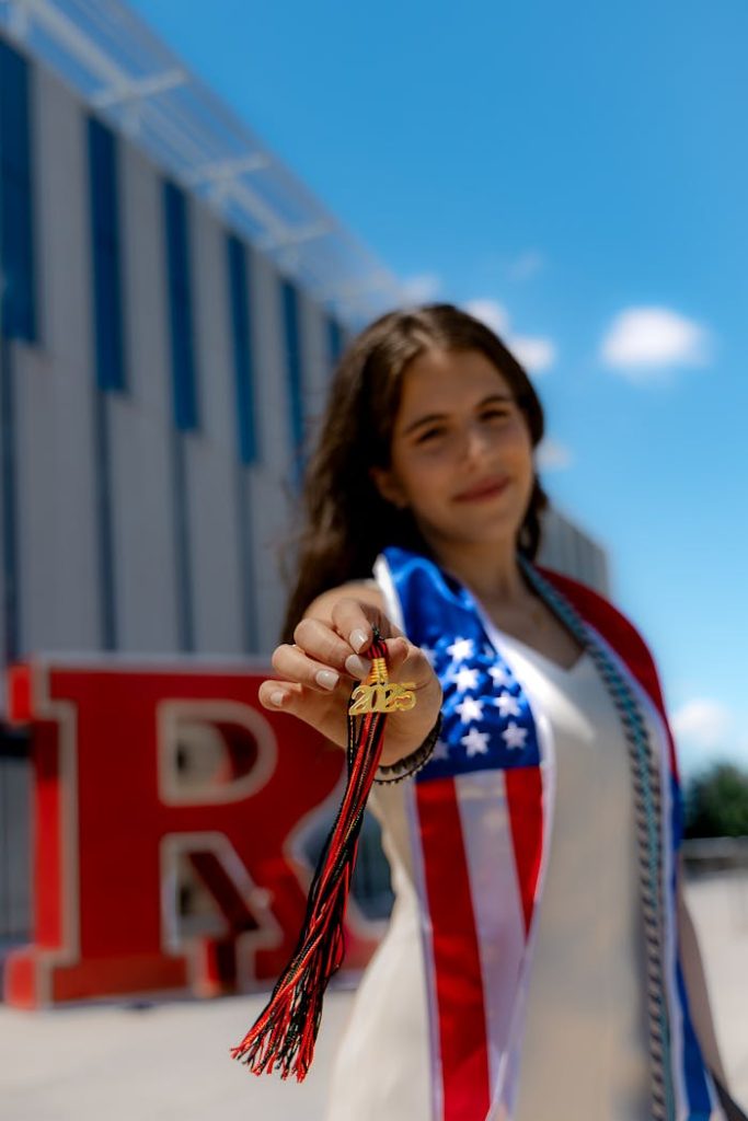 pexels-photo-32062248 Graduate holding tassel in front of Rutgers R block, New Brunswick, NJ.